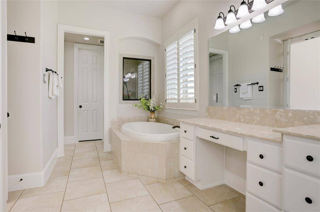 Indulge in this bathroom’s soaking tub, expansive vanity, and elegant finishes. Natural light and soft tile flooring create a peaceful, refined atmosphere.