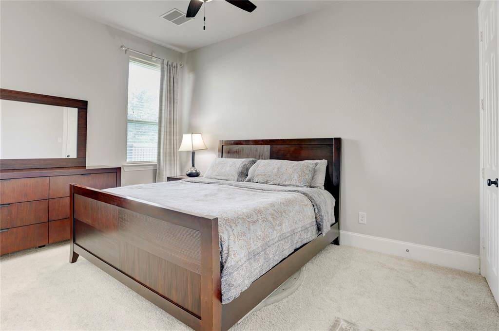 This inviting bedroom features neutral carpet, a warm wood bed set, and a window that fills the space with natural light. A ceiling fan adds comfort.