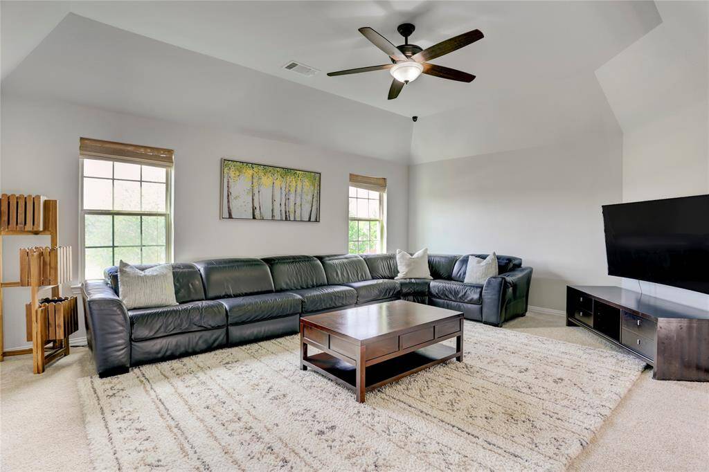 Relax in this expansive living room with vaulted ceilings, a sectional sofa, ceiling fan, and abundant natural light. A cozy rug and sleek media setup round out the space.
