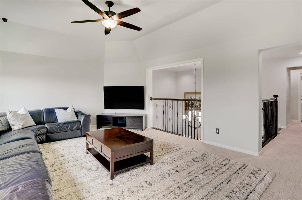 This spacious living area offers plush seating, high ceilings, and neutral tones. A hallway with iron railings adds architectural interest and flow.