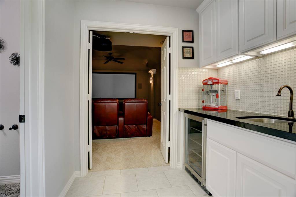 A cozy media room with oversized chairs and a large screen sits next to a compact kitchenette with sleek counters and cabinetry—ideal for movie nights and snacks.