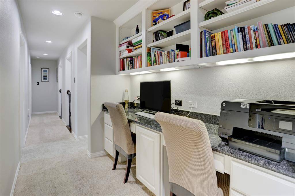 A built-in workspace with shelves, a desk, and ample lighting offers a functional home office setup along a bright hallway.