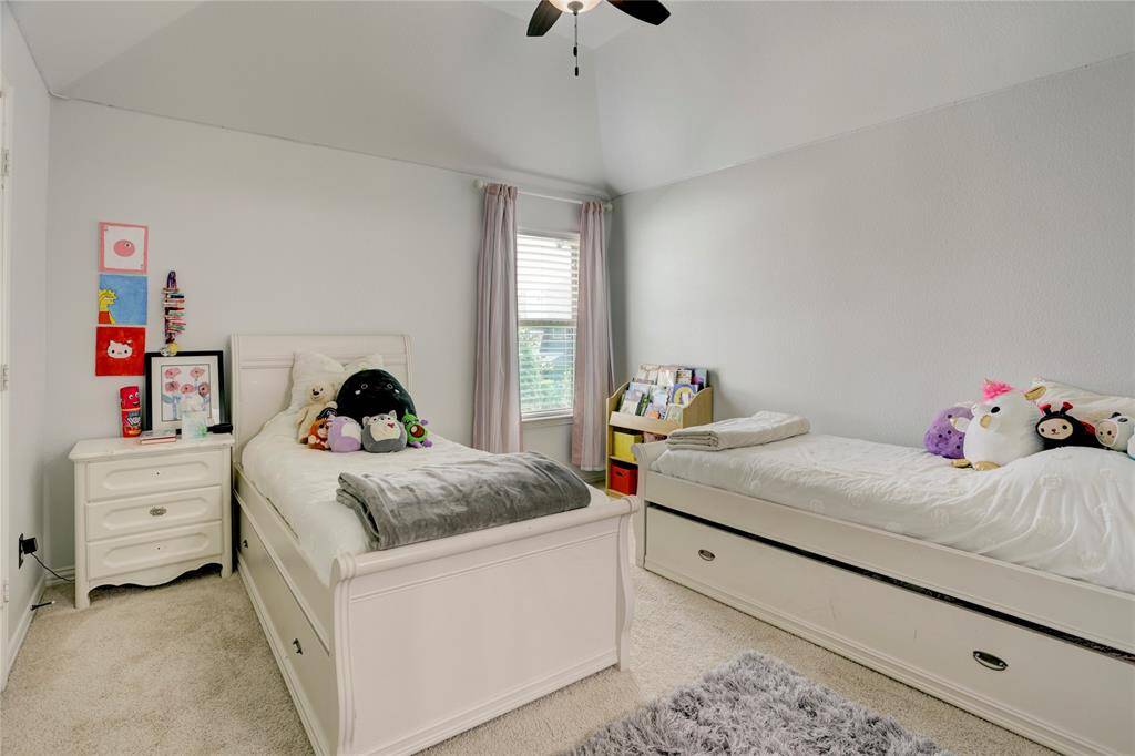 This cheerful bedroom with twin beds, a soft carpet, and ceiling fan is ideal for play or rest. Light curtains and a bookshelf complete the space.