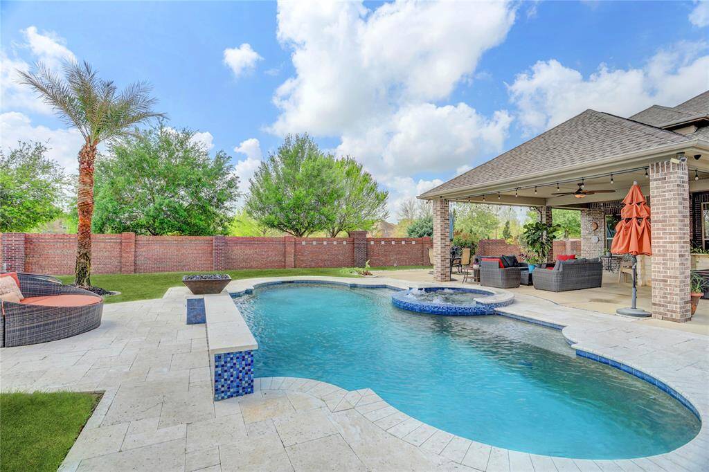 This backyard boasts a sparkling pool and integrated spa, a covered lounge area, and tropical landscaping framed by a privacy wall. A true outdoor haven.