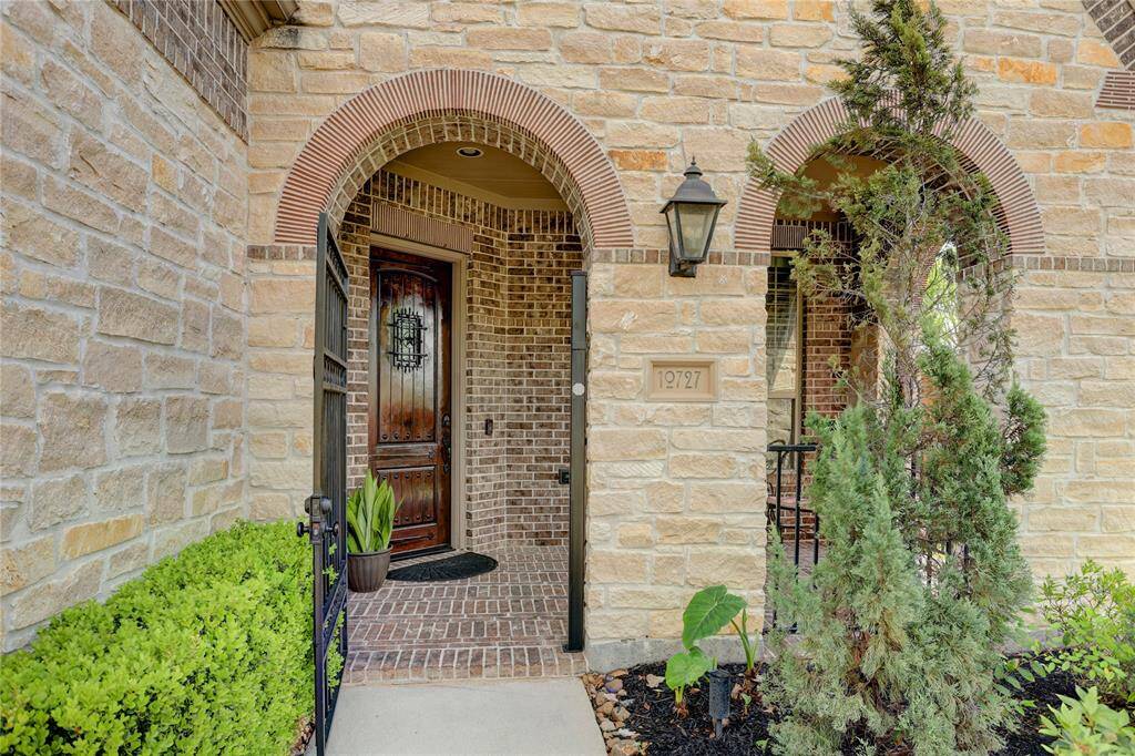 An arched stone entry with a decorative wood door and iron gate sets a welcoming tone. Framed by greenery and a soft porch light, this entrance hints at the charm found inside.