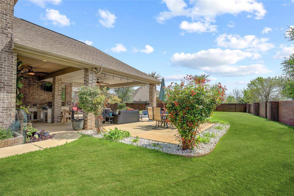 A lush backyard retreat with covered dining, built-in kitchen, and a manicured lawn—designed for effortless entertaining and relaxation.