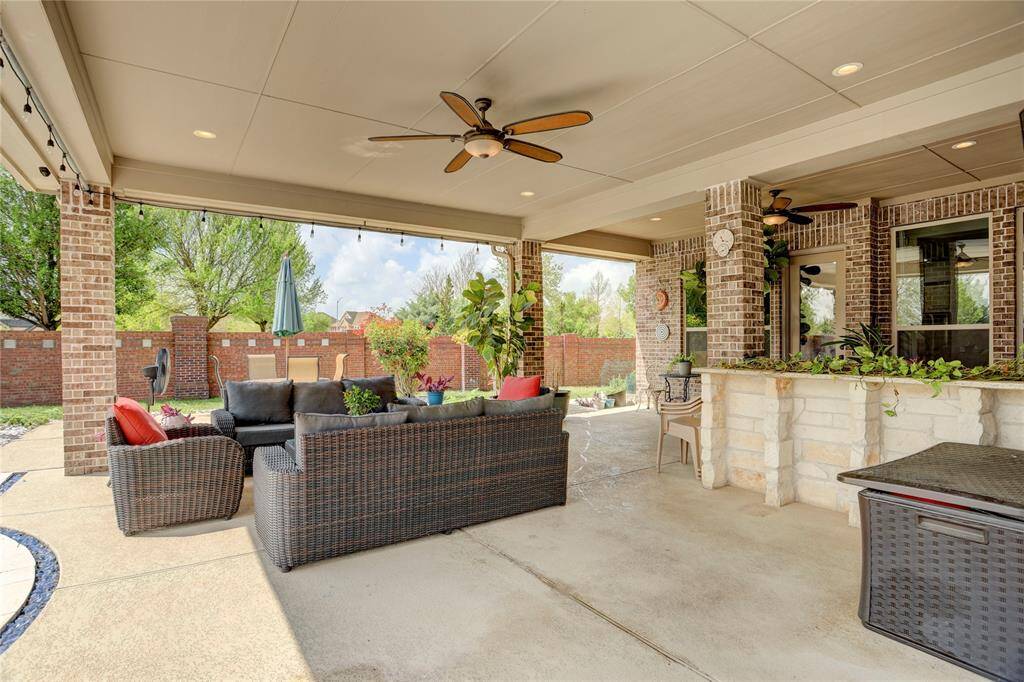 Brick details and ceiling fans enhance this covered patio with seating and a built-in bar. A tranquil view of the landscaped yard completes the scene.