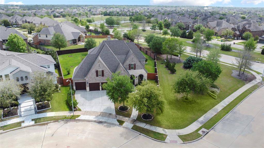 An aerial view reveals a stately two-story brick home on a generous corner lot. A wide drive, mature trees, and manicured landscaping enhance its residential appeal.
