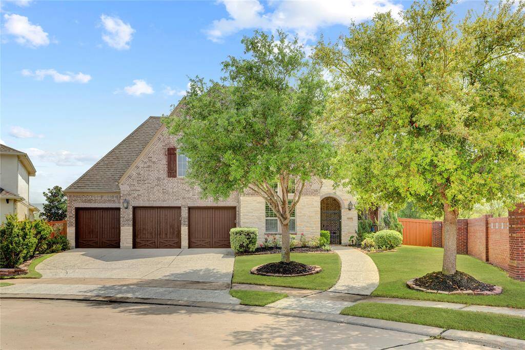Curb appeal abounds with this two-story brick home featuring a three-car garage, manicured lawn, and mature trees lining the property.