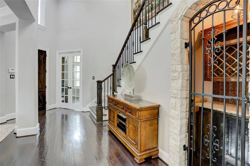 This refined entry area showcases dark hardwood floors, a wrought iron staircase, and a stone-accented wine nook. Natural light pours in from the nearby French doors.