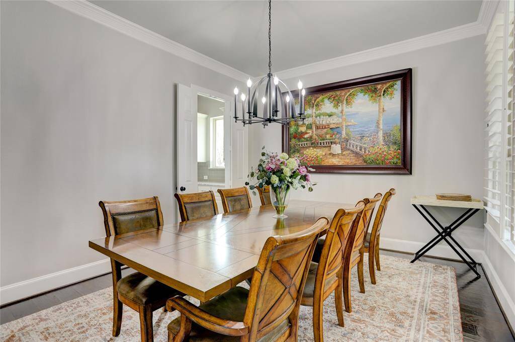 Gather in style in the formal dining room featuring a rich wood table, statement chandelier, and a striking landscape painting. A large window and light color palette add brightness and charm.