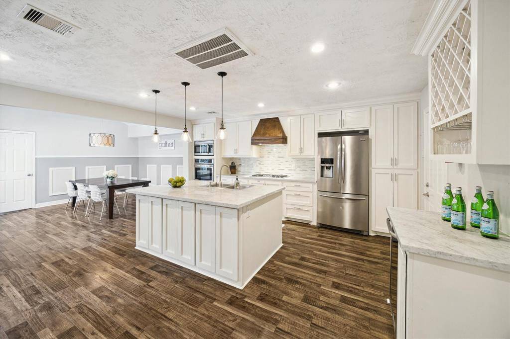Well-appointed kitchen features an oversized island, stainless steel appliances, a custom backsplash, and a 5-burner gas cooktop.