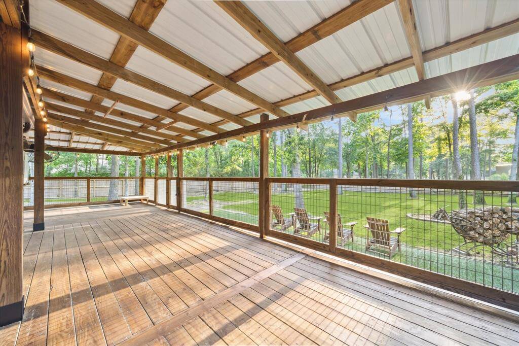 This spacious, covered wooden deck offers a serene view of a lush, tree-filled backyard.