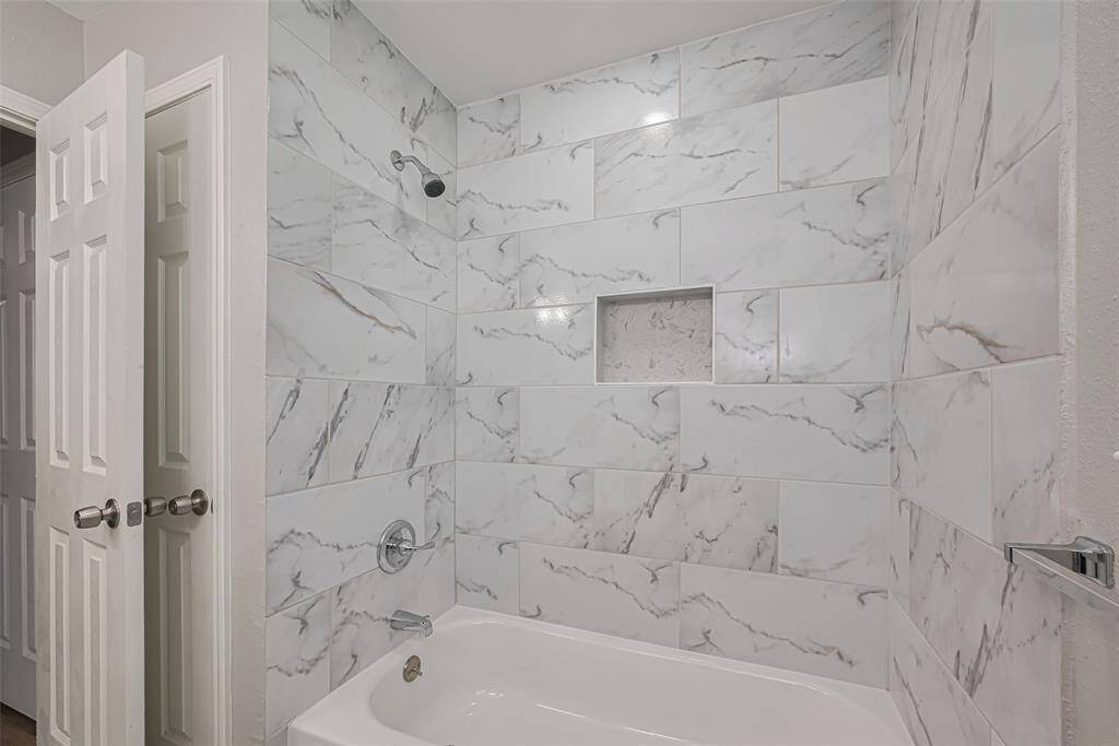 This full bathroom includes a tub-shower combo surrounded by the same tasteful gray-and-white tilework seen throughout.
