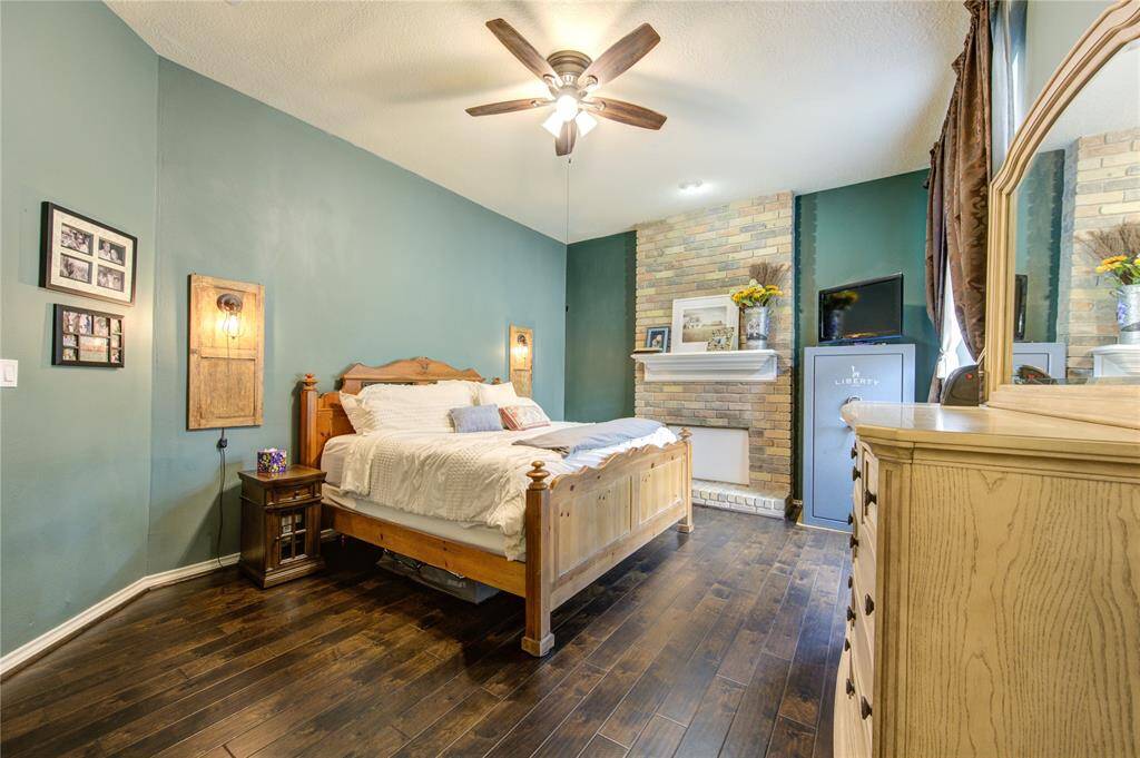 This cozy Primary Bedroom features luxury vinyl plank flooring, a stylish teal accent wall, and a ceiling fan. It has a rustic wooden bed, a brick fireplace, and ample natural light from large windows and located on the first floor