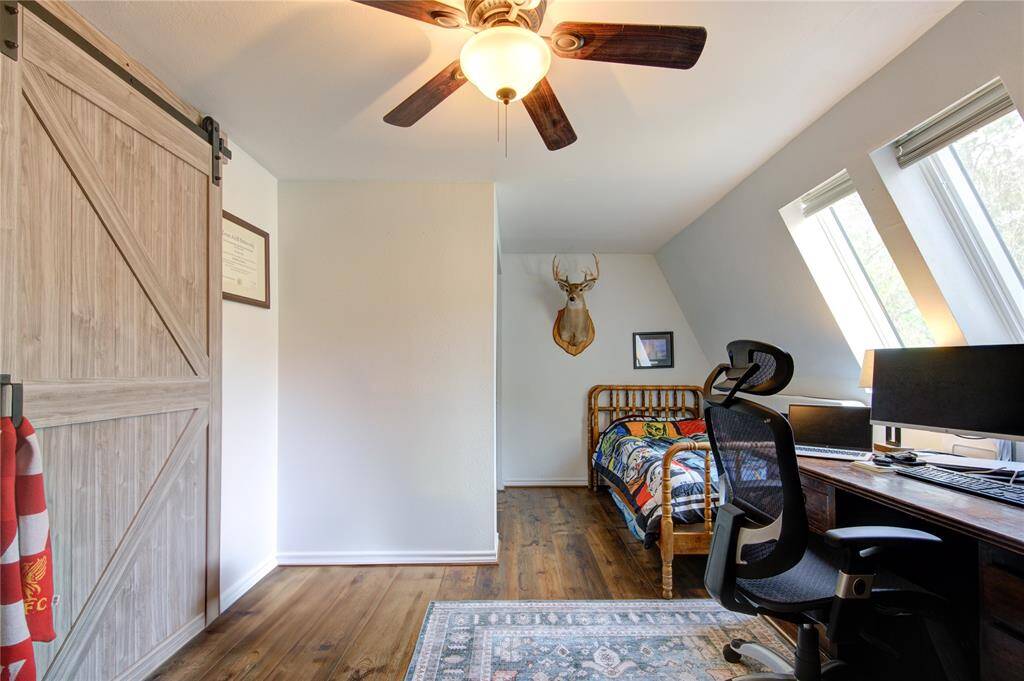 This cozy bedroom/game room features a wooden sliding barn door, luxury vinyl plank flooring, and ample natural light from large skylights.