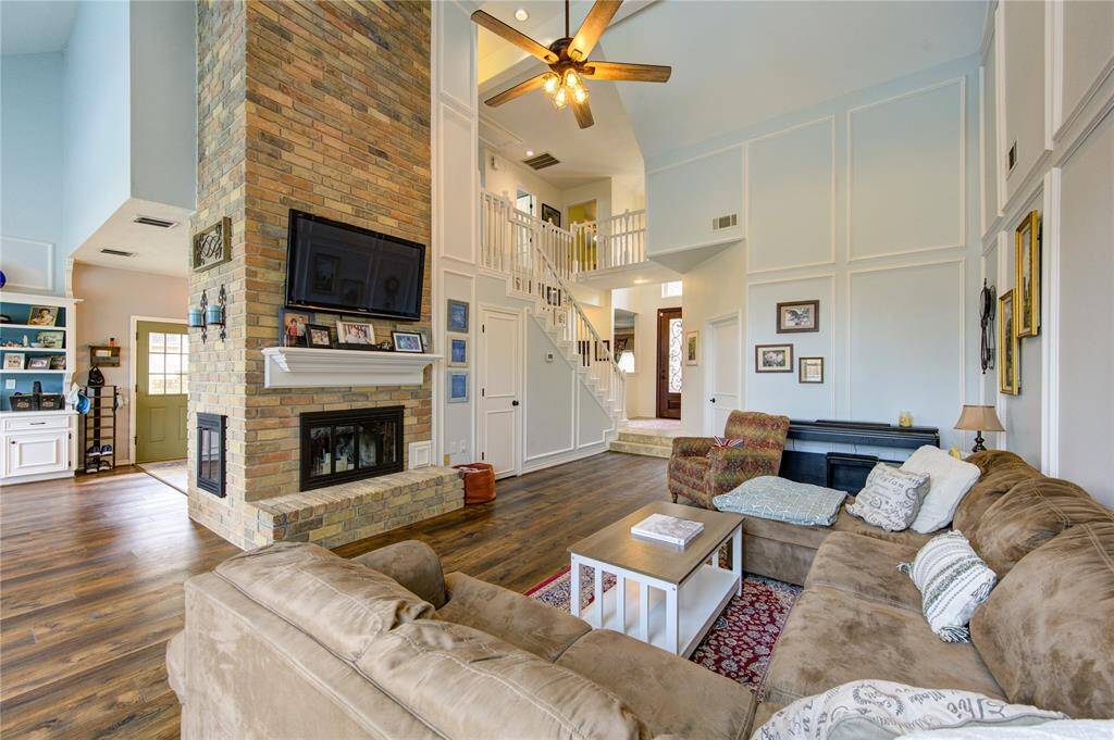 This spacious living room features high ceiling and a cozy brick fireplace.   The open layout connects to a bright kitchen area, while a staircase leads to the upper level, enhancing the airy feel.