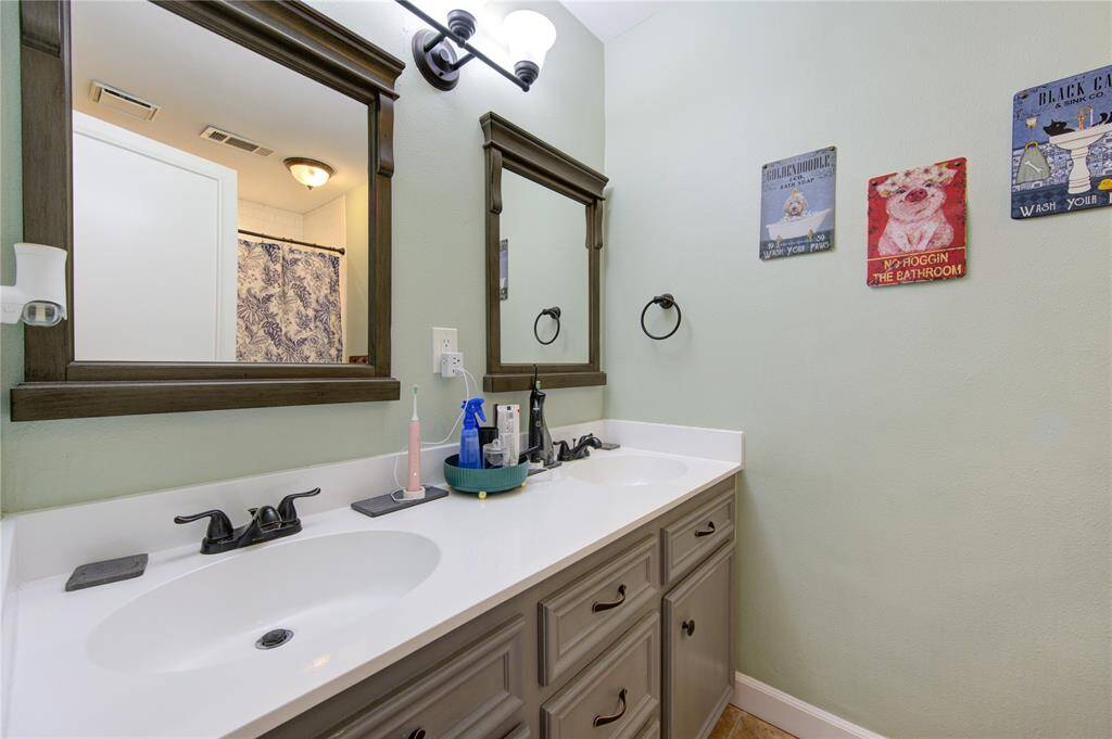 This bathroom features a extended vanity with dark wood-framed mirrors and modern faucets. The walls are painted a soft green