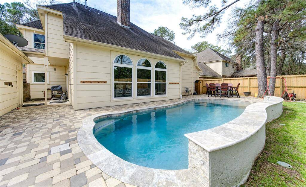 This photo showcases a charming backyard with a lovely 2 year old in-ground pool, surrounded by an extended paved patio area. The house features large arched windows overlooking the pool, offering a perfect blend of indoor and outdoor living.