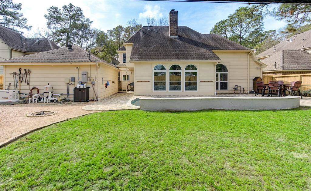 This photo showcases the backyard of a charming two-story home with a spacious patio, perfect for outdoor entertaining. The well-maintained lawn and surrounding trees offer a serene atmosphere, while the large, arched windows provide ample natural light to the interior. The home also comes equipped with a full home generator.