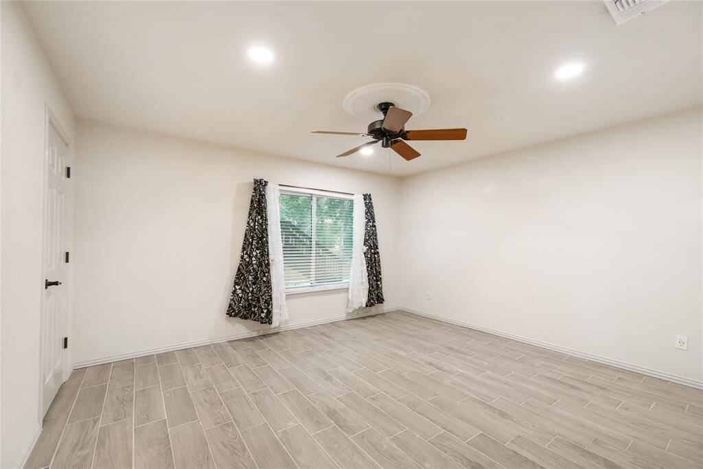 This bright and comfortable secondary bedroom features wood-look tile floors and a large window that keeps the space feeling open and airy.