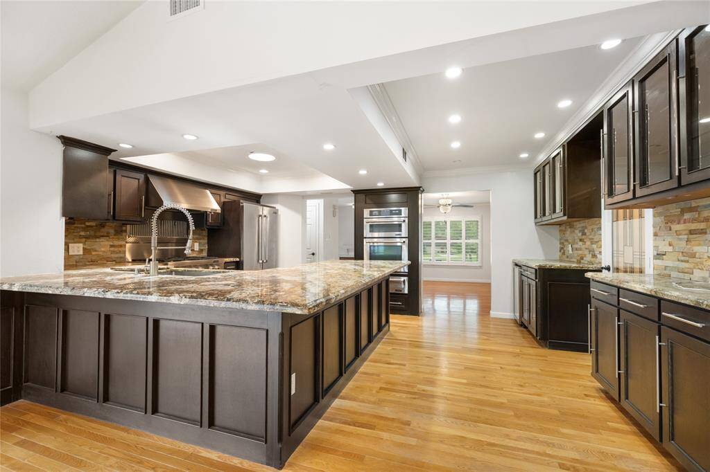The kitchen pairs dark, richly toned cabinetry with striking marble countertops and a textured stone backsplash, creating a space that feels both grounded and elevated. Thoughtful finishes give the kitchen a custom feel.