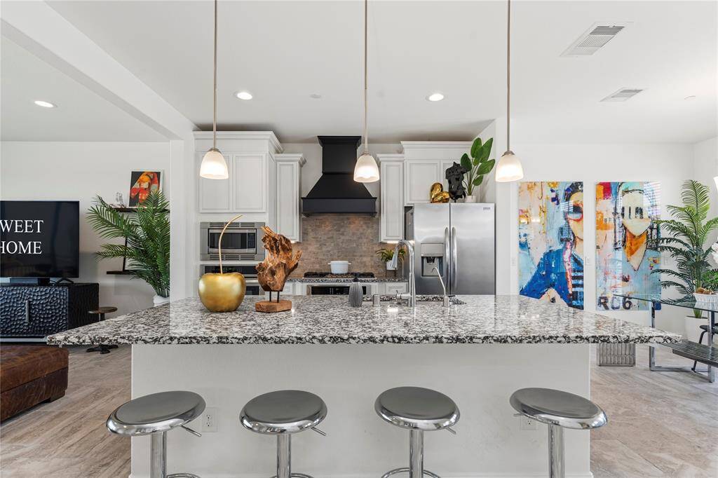 Cook in style with this 5 burners stainless gas range and sleek designer custom vent hood. Set against a neutral stone backsplash, undermount lighting and surrounded by white custom cabinetry, this area combines modern luxury with practical ease.
