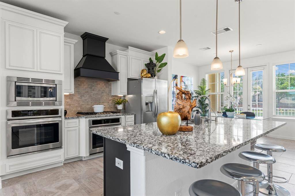 This stunning kitchen island offers extended granite countertops, stylish pendant lighting, and seating for five—perfect for casual dining or entertaining, all while enjoying views from multiple sun-filled windows.