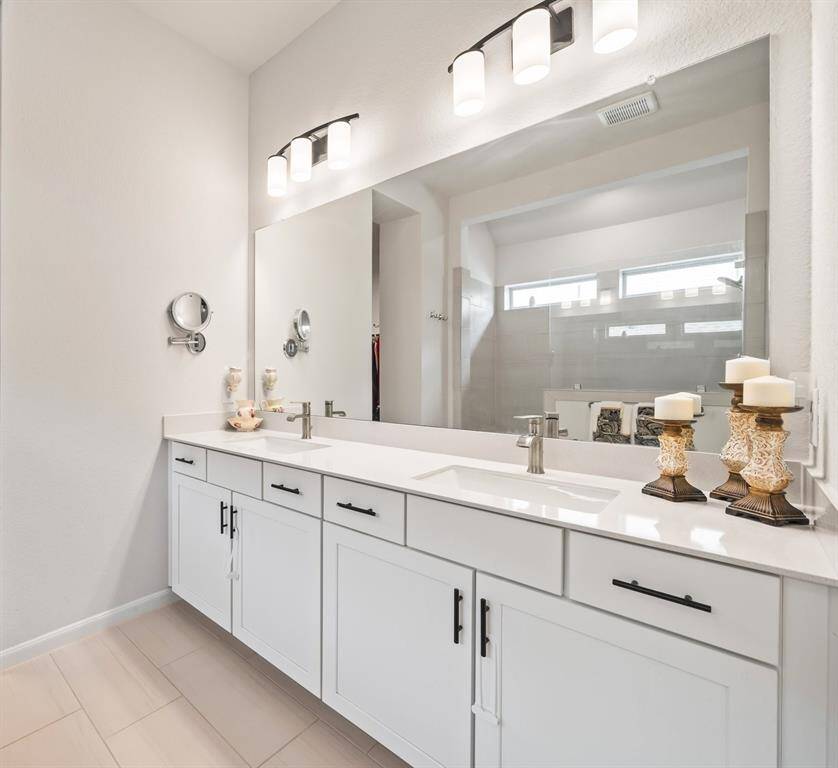 Primary bathroom is complete with dual sinks and super shower shown in the mirror's reflection.
