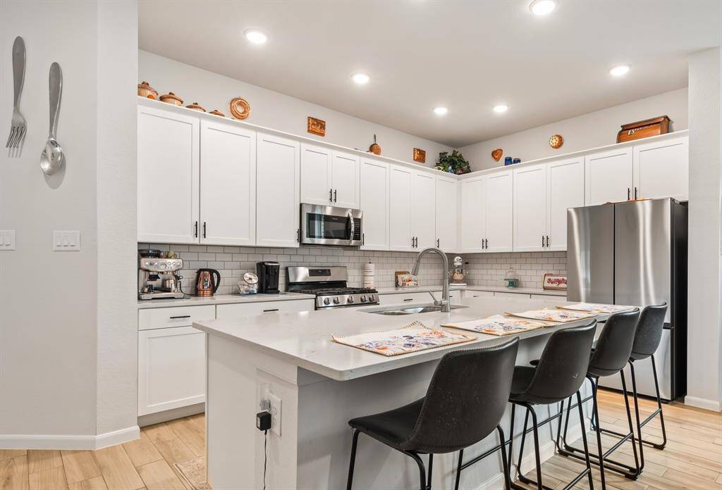 All white kitchen cabinets, subway tile backsplash, Gas stove, and a breakfast bar at the island.