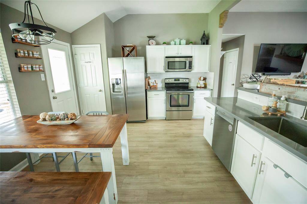This bright and modern kitchen blends functionality with farmhouse charm. Crisp white cabinetry is paired with quartz countertops and stainless steel appliances, including a side-by-side refrigerator, oven, microwave, and dishwasher.