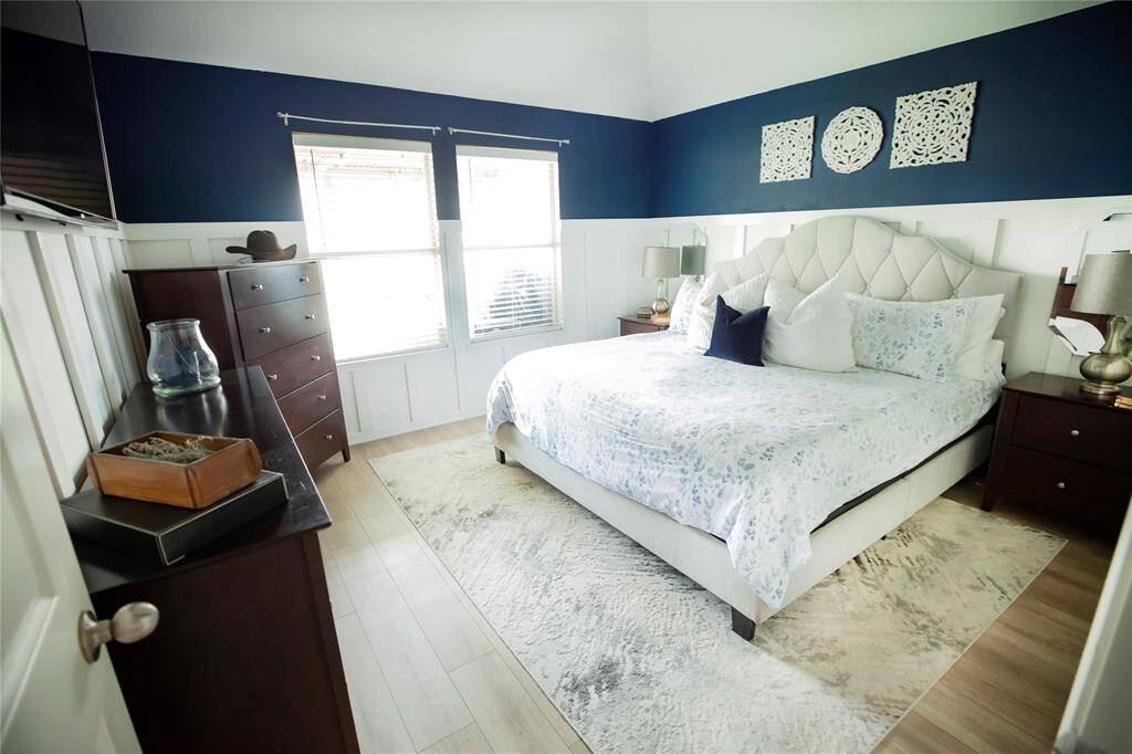 This inviting master suite offers a peaceful retreat, thoughtfully updated with modern finishes and fresh design. The bedroom features soft two-tone walls with rich navy above crisp white wainscoting, complemented by warm wood-look flooring.