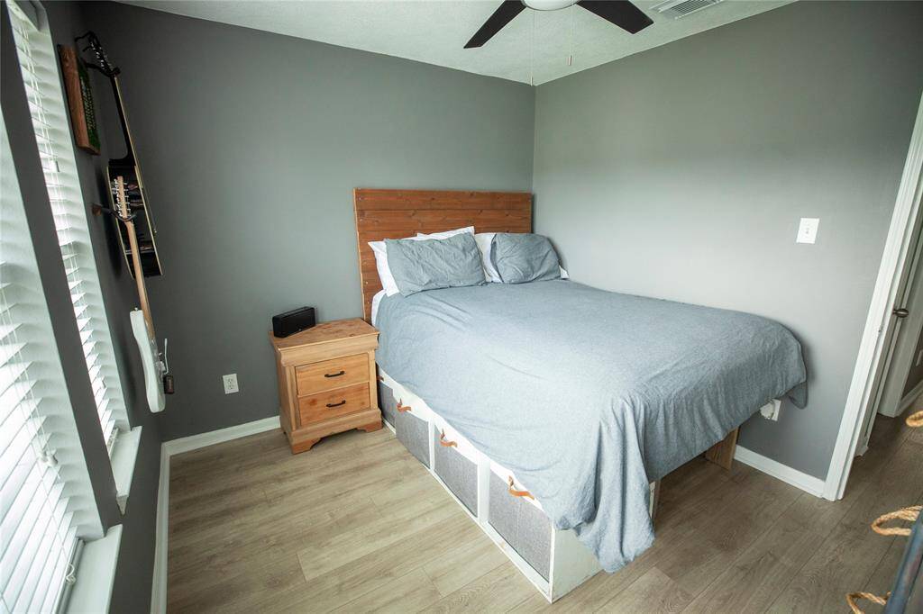 This recently painted secondary bedroom features clean, modern tones with soft gray walls and matching wood-look flooring that creates a warm, cohesive atmosphere.