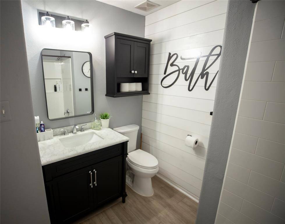 This secondary bathroom has been freshly painted and beautifully updated. It features a sleek black vanity with a white marble countertop, offering both elegance and functionality. The vanity is paired with a modern mirror and three-bulb vanity light, adding brightness to the space. A black wall-mounted cabinet provides additional storage above the toilet.