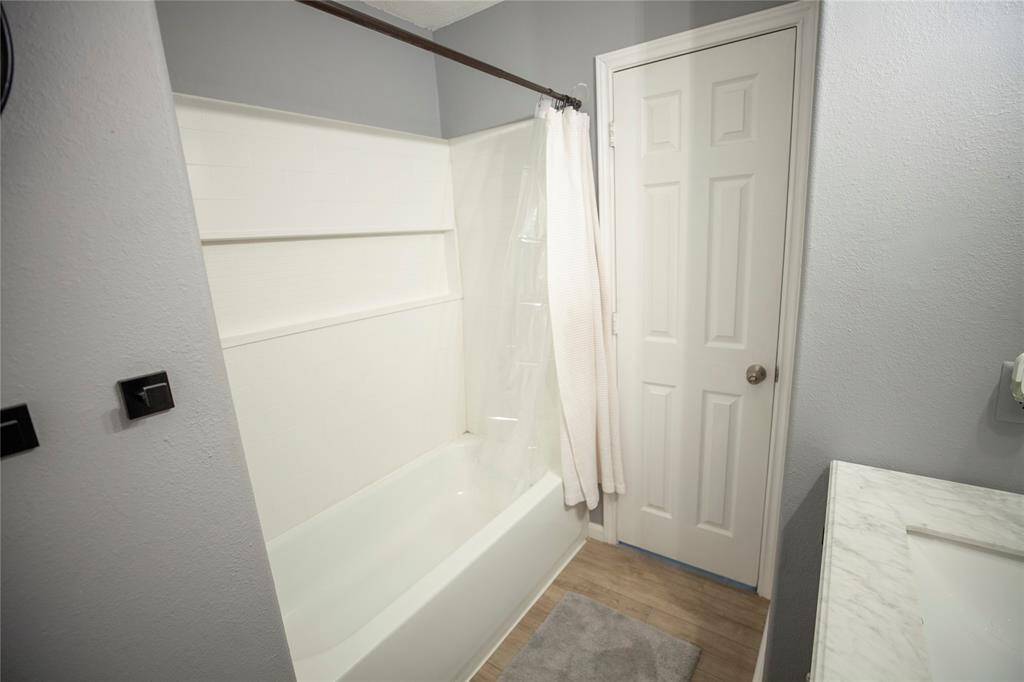 The shower/tub combo has a clean white tile surround with built-in shelving and a simple curtain rod, blending style with practicality.