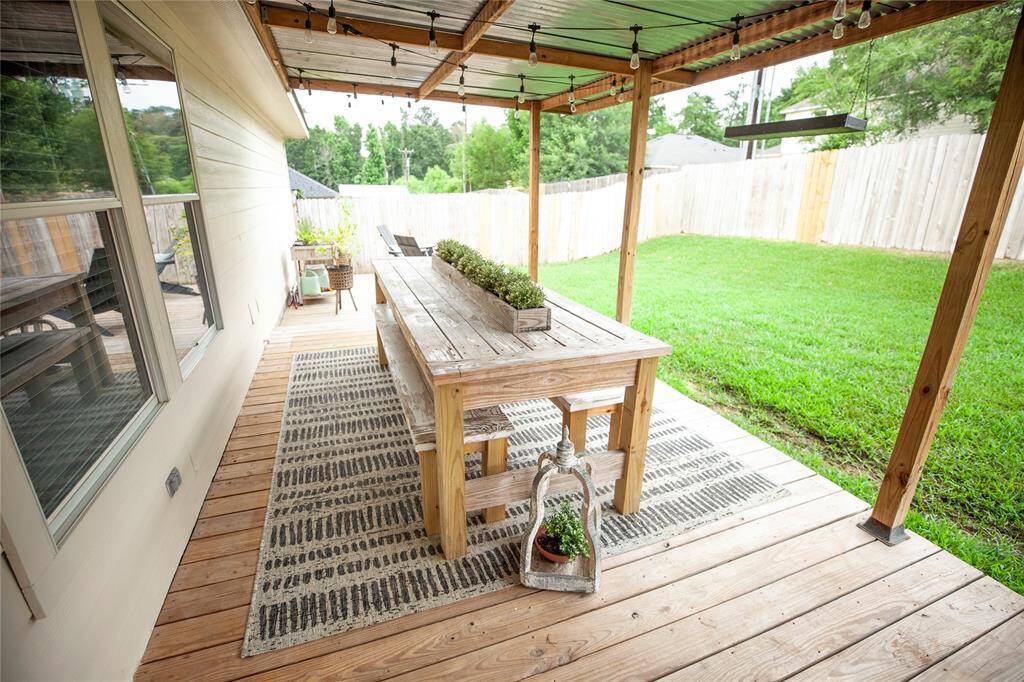 The covered section includes string lights for evening ambiance, a cozy seating area with a fire pit, and a long rustic dining table perfect for hosting meals or gatherings.
