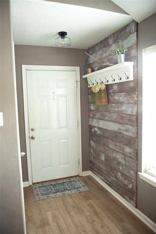 This photo showcases a stylish and welcoming entryway featuring warm wood-look flooring and soft neutral walls. A rustic accent wall with weathered wood planks adds texture and charm.