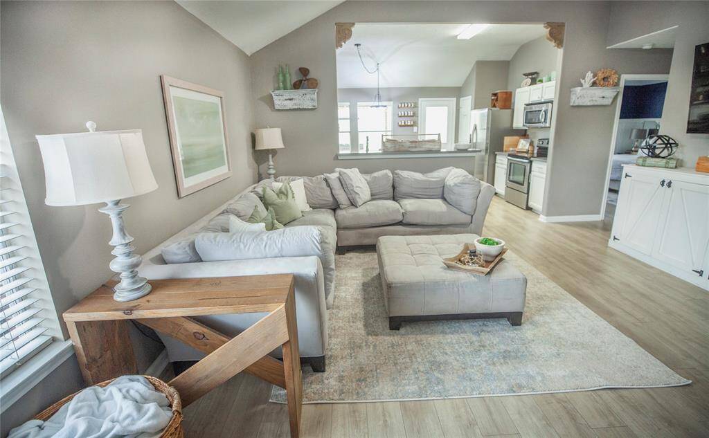 This bright and airy living room features a neutral color palette with soft gray walls, warm wood-look flooring, and high vaulted ceilings that create a spacious feel.