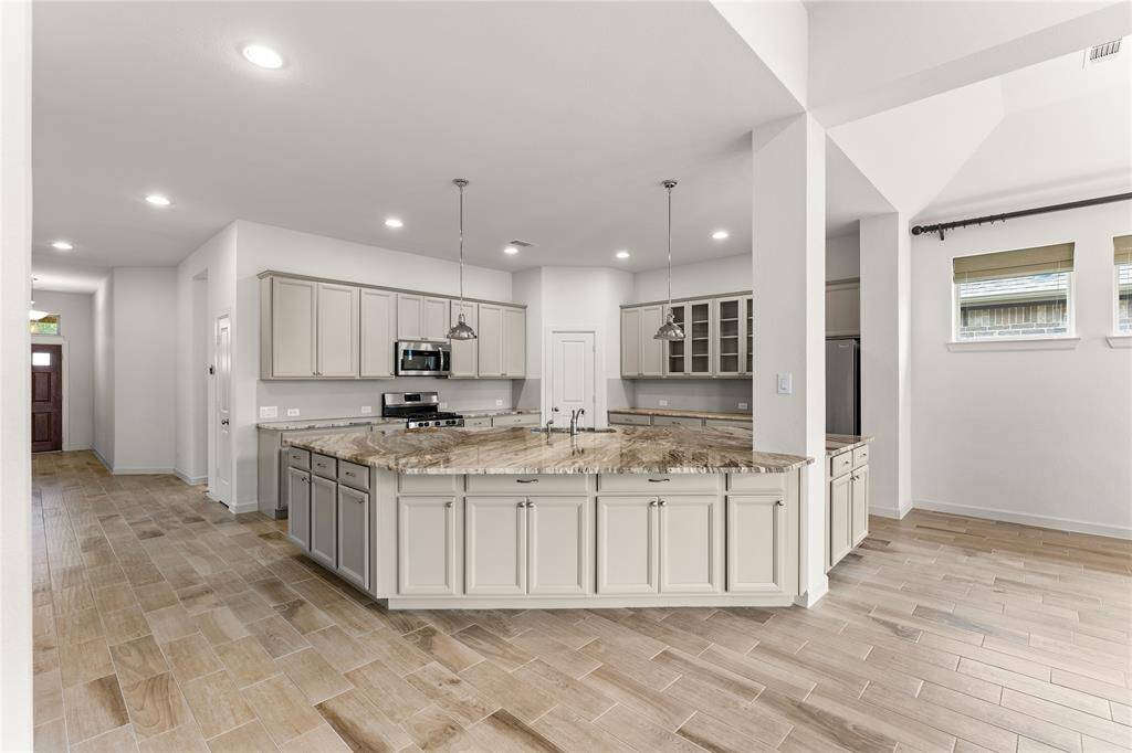 Chef’s kitchen features a spacious island, white cabinetry, stainless appliances, and a gas cooktop.