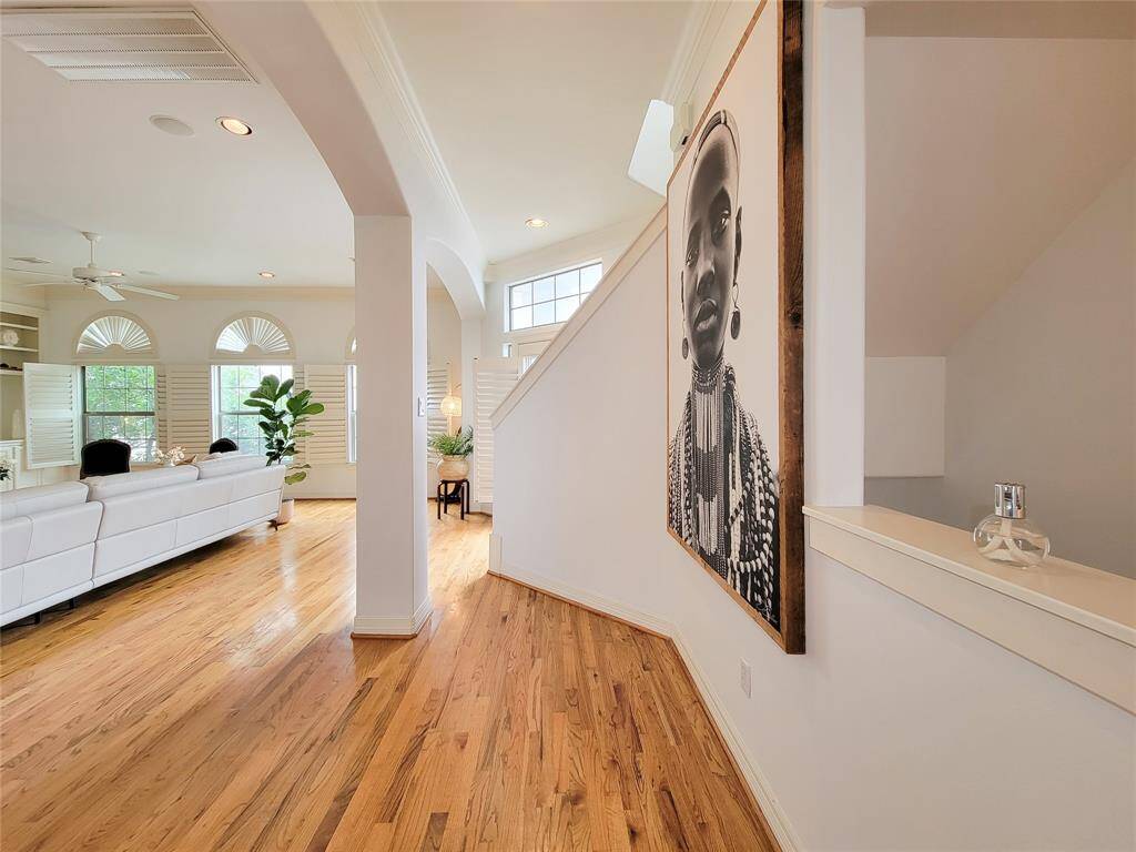 This photo showcases a bright, open-concept living space with hardwood floors, large windows with shutters, and a stylish staircase. The room features modern decor, including a large wall art piece and white furnishings, creating a welcoming and contemporary atmosphere.