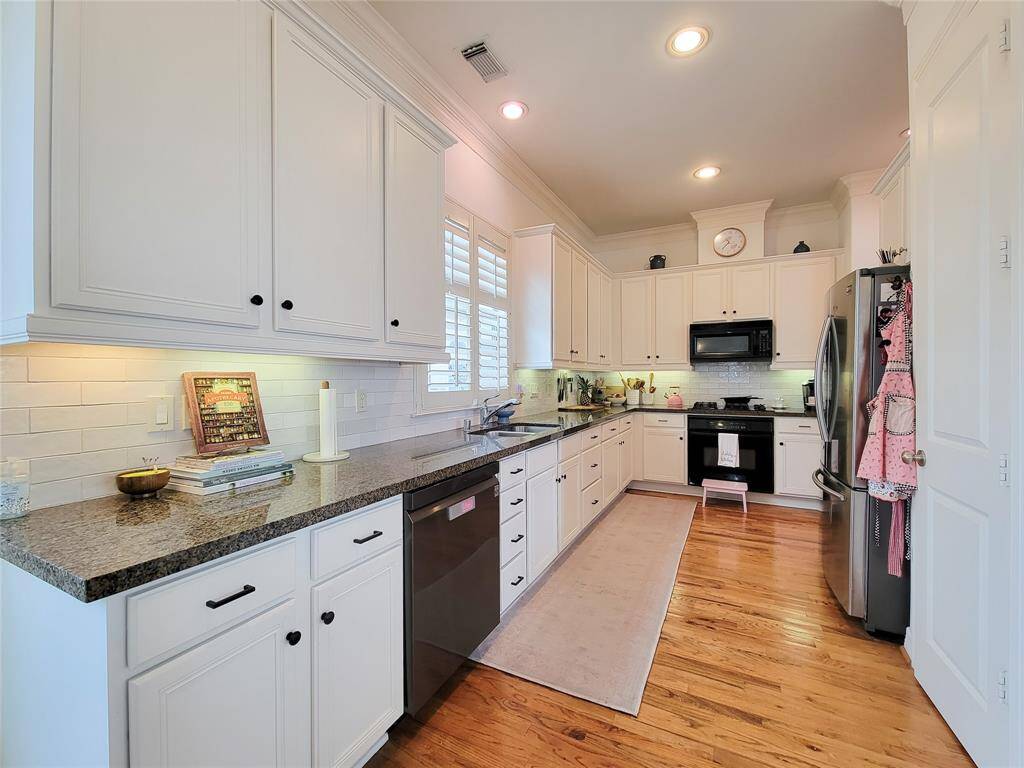 This spacious kitchen features modern stainless steel appliances, ample white cabinetry and granite coutertops. The hardwood floors and recessed lighting enhance its warm, inviting atmosphere.