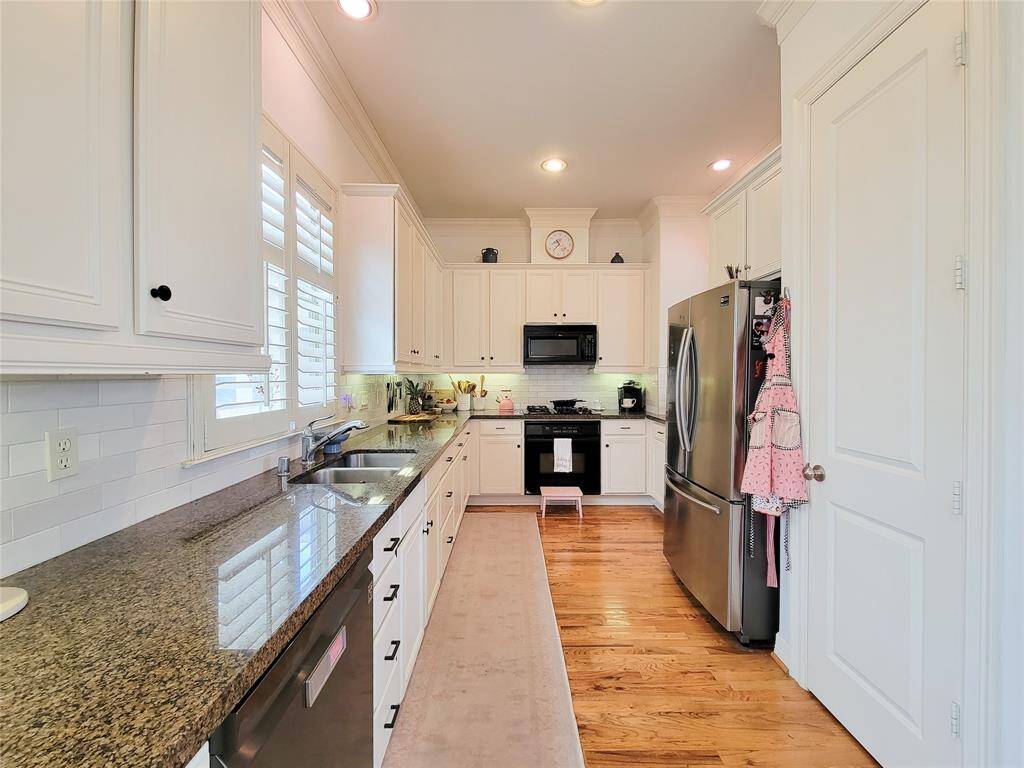 Bright, inviting kitchen with granite countertops, white cabinetry, stainless steel appliances, and hardwood floors. Cozy and functional layout with ample storage and natural light.