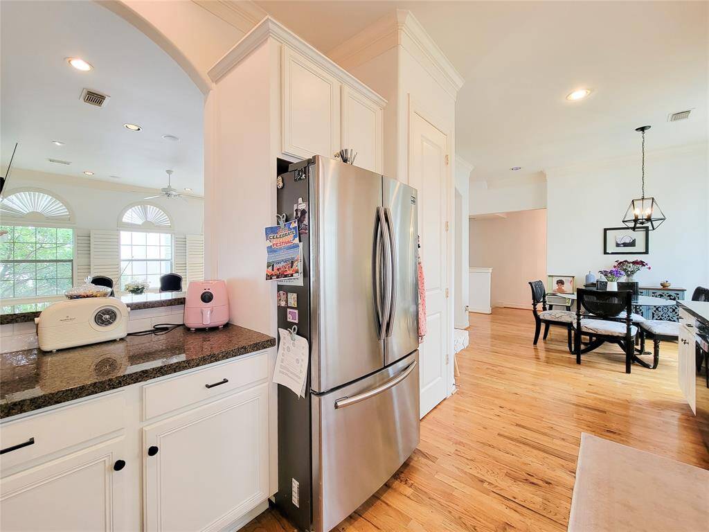 This bright kitchen features stainless steel refrigerator, hardwood floors, and ample counter space. An adjacent dining area with a modern light fixture offers a welcoming space for meals. Large windows allow plenty of natural light, enhancing the open and airy feel.