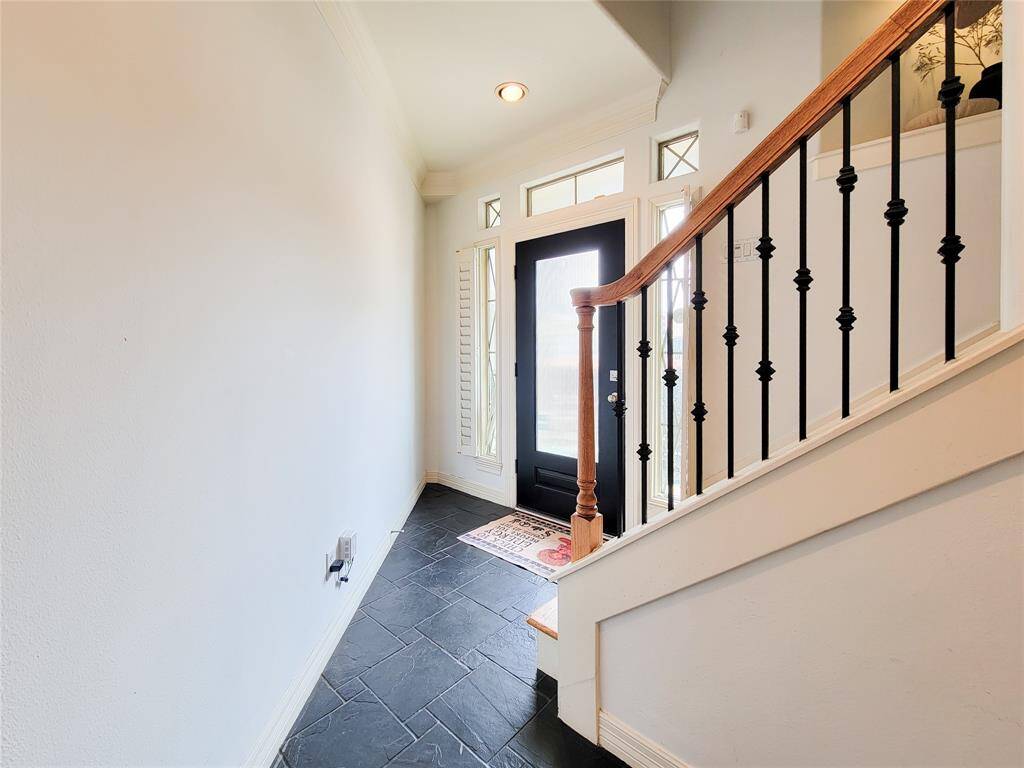 This welcoming tiled entryway features a modern black front door with glass panels, offering natural light. The space is accented by a staircase with elegant iron balusters and a wooden handrail,