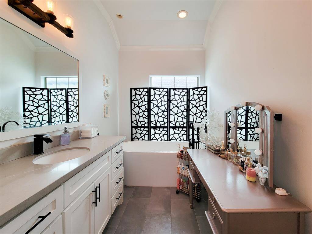 Bright bathroom with modern decor featuring a spacious vanity, elegant fixtures, and a unique patterned window screen. The space includes a large mirror and ample countertop area for personal items.