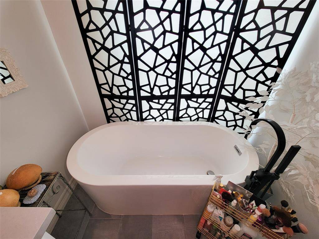 This bathroom features a modern, freestanding white bathtub against a striking geometric black and white accent wall. The space is complemented by sleek fixtures and a variety of neatly organized toiletries, offering a stylish and functional setting.