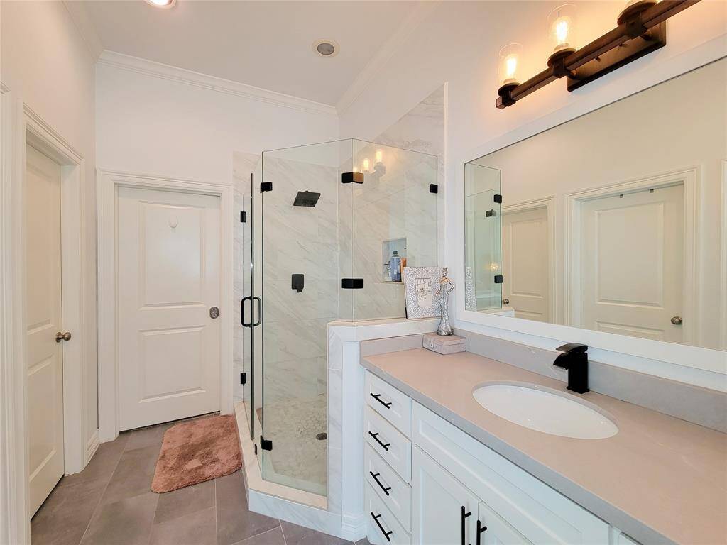 This bathroom features a modern design with a glass-enclosed shower, white cabinetry, a sleek countertop with a black faucet, and elegant lighting fixtures.
