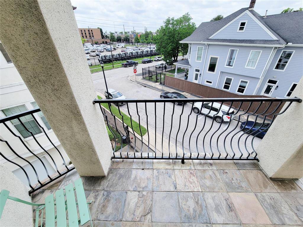 This photo showcases a small balcony with a stylish metal railing and tiled flooring. It offers a view of a residential street with parked cars and neighboring homes, providing a cozy outdoor space in an urban setting.