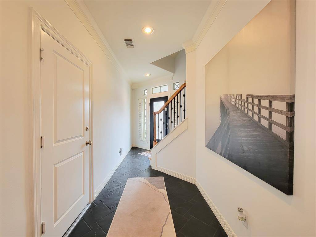 This photo showcases a bright, inviting entryway with a tiled floor, modern staircase, and a large wall art piece. The space is well-lit with recessed lighting and a transom window above the door, creating a welcoming atmosphere.