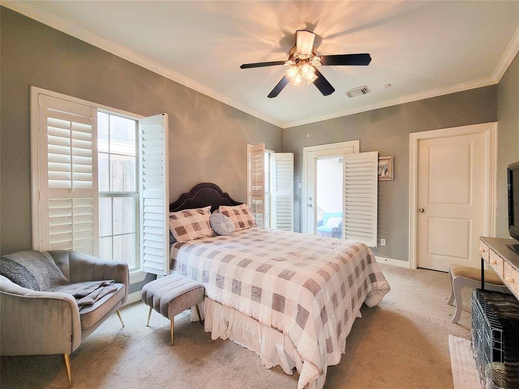 First floor spacious bedroom with soft gray walls and ample natural light from large windows with shutters. Glass door leading to small private patio and greenspace.